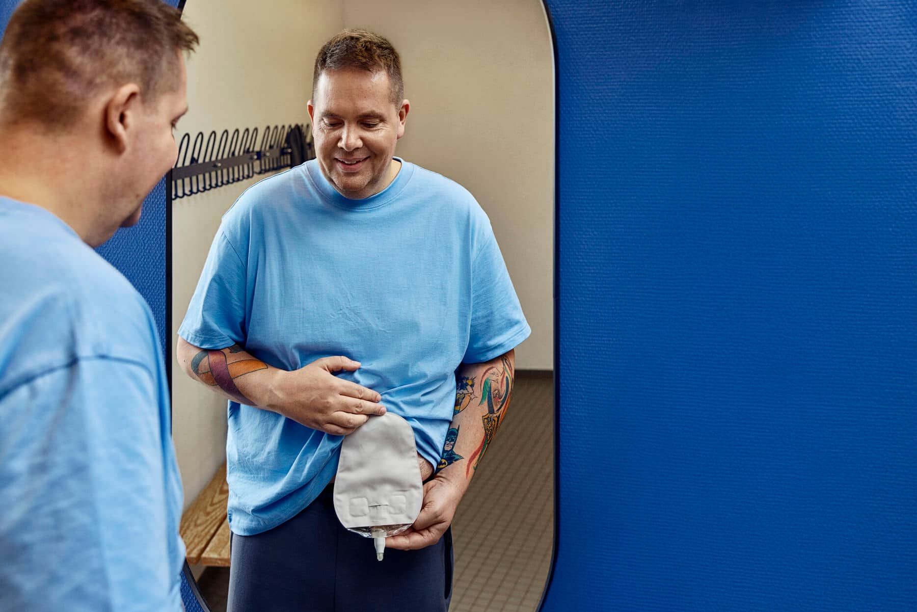 Homme tenant une poche d'urostomie devant un miroir